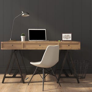 May include: A wooden desk with a laptop, lamp, and small potted plant. A white chair sits in front of the desk. The desk has metal legs and drawers. A framed picture and a wire basket are also visible.