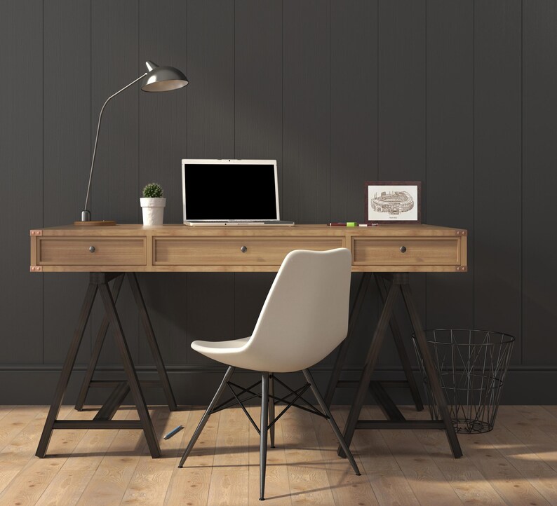 May include: A wooden desk with a laptop, lamp, and small potted plant. A white chair sits in front of the desk. The desk has metal legs and drawers. A framed picture and a wire basket are also visible.