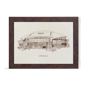 May include: A framed print of AT&T Stadium, rendered in sepia tones. The stadium's architectural details are visible in the illustration. The frame is a dark brown color. The text "AT&T Stadium" is printed below the image.