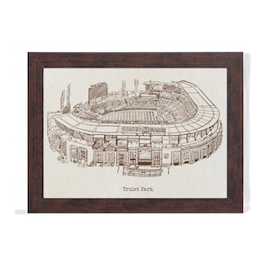 May include: A framed print featuring a detailed sketch of Truist Park, a baseball stadium. The artwork is in sepia tones, showcasing the stadium's architecture, including the seating, field, and scoreboard. The frame is a dark brown color.