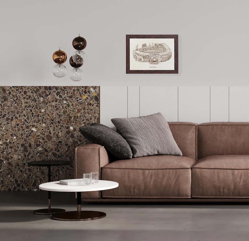 May include: A modern living room featuring a brown leather sofa with two decorative pillows. A framed architectural drawing hangs on the wall. A white and black coffee table sits in front of the sofa, and a decorative light fixture hangs from the ceiling.