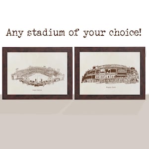 May include: Two framed stadium prints. One depicts Dodger Stadium, the other Wrigley Field. Both are brown line drawings on cream-colored paper, set in dark brown frames. Text above reads "Any stadium of your choice!"