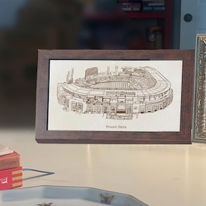 May include: A framed print of Truist Park, a detailed architectural illustration in sepia tones. The stadium is depicted with intricate lines, showcasing its structure. The frame is a dark brown, adding a classic touch to the artwork.