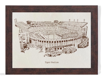 Puede incluir: Una impresión enmarcada del estadio Tiger, con una detallada ilustración a pluma y tinta del estadio. La obra de arte está en tonos marrones y beige, con el texto "Tiger Stadium" en la parte inferior. El marco es de color marrón oscuro.