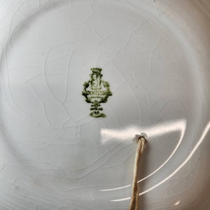 May include: A white ceramic plate with a green mark that reads "Factory of Pont-l'Abb&eacute;" in French. The plate has a hole in the bottom with a string attached.