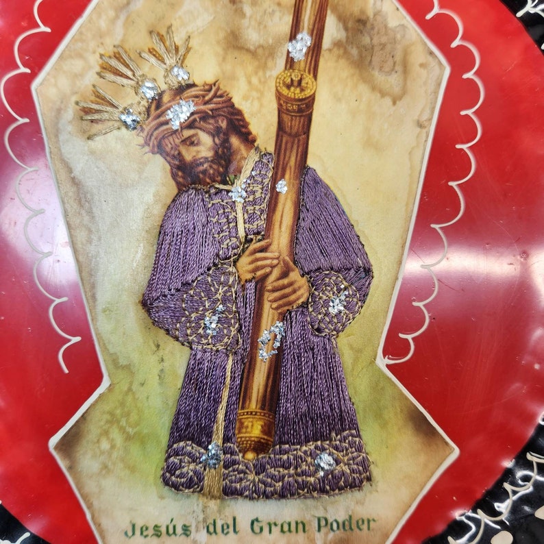 May include: A religious image of Jesus carrying a cross, with a crown of thorns on his head. The image is on a red background with a scalloped border. The text "Jes&uacute;s del Gran Poder" is at the bottom of the image.