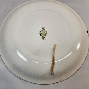 May include: White ceramic plate with a green and gold logo that reads "G.N.I.S.S.A.N." The plate has a string attached to the bottom.