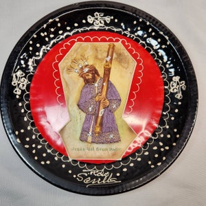 May include: Black and white ceramic plate with a red center featuring a religious image of Jesus holding a staff. The image is surrounded by a white scalloped border and the text "Jesus del Gran Poder" and "Seville".