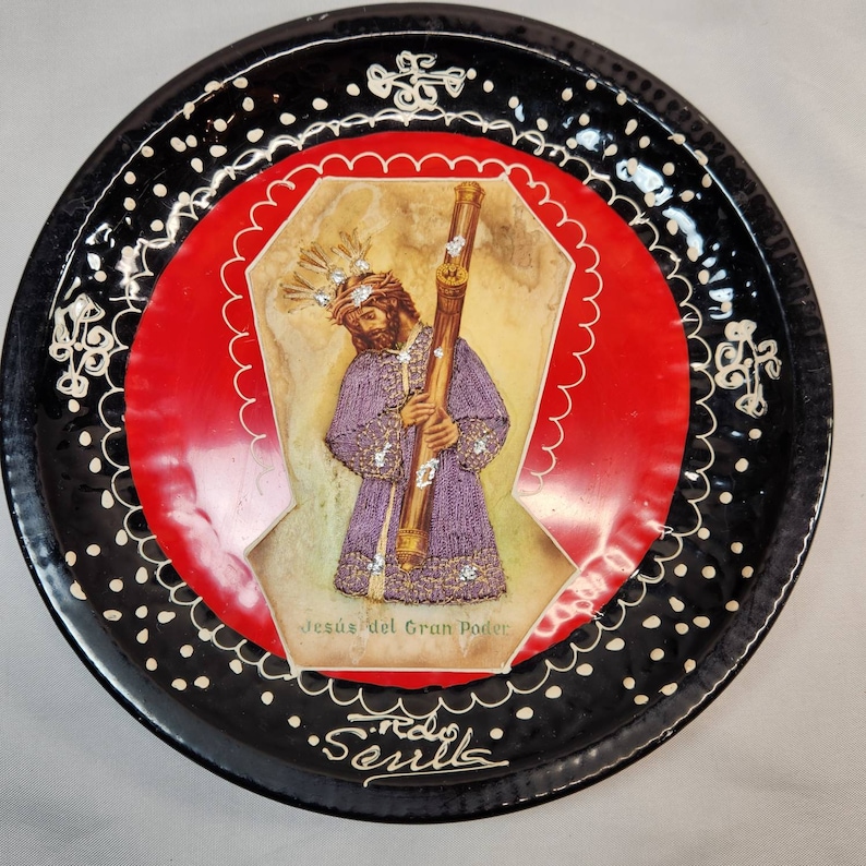 May include: Black and white ceramic plate with a red center featuring a religious image of Jesus holding a staff. The image is surrounded by a white scalloped border and the text "Jesus del Gran Poder" and "Seville".