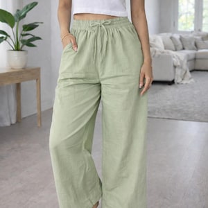May include: A person wearing a white crop top and light green wide-leg pants with a drawstring waist. The pants have pockets. The person is standing barefoot on a light gray floor.