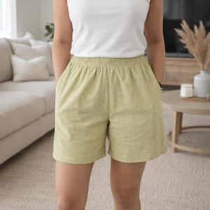 May include: A person wearing a white tank top and light green shorts with pockets. The shorts have an elastic waistband. The outfit is casual and suitable for warm weather.