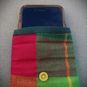 May include: A red, green, and yellow plaid phone case with a yellow button. The case is made of fabric and has a dark green trim.