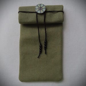 May include: A green canvas pouch with a black drawstring and a decorative button. The button has a geometric design in shades of green, blue, and white.