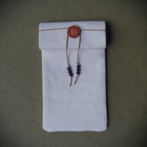 May include: A white fabric pouch with a wooden flower embellishment and purple beads. The pouch is tied with twine.
