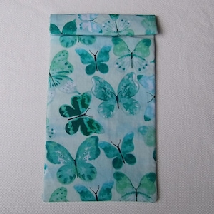 May include: A rectangular, folded fabric case with a light blue background and a pattern of teal and green butterflies. The butterflies vary in size and have detailed wing patterns. The top of the case is folded over.
