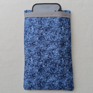 Könnte beinhalten: Eine blaue Handyhülle aus Stoff mit einem wirbelnden Blumenmuster. Die Hülle hat eine graue obere Zierleiste und hält ein Smartphone. Der Stoff ist mittelblau mit dunkleren blauen Wirbeln.