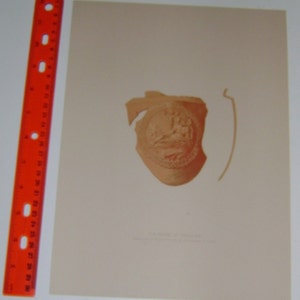 May include: A close-up of a broken terracotta fragment with a raised design of a bird and a floral motif. The fragment is a light brown color and is on a white background.