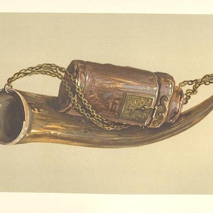 May include: A brown horn with a metal container attached to it with a chain. The container has a decorative design and a lock.