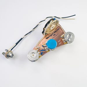 May include: A guitar wiring harness with a copper-colored base, three knobs, and a switch. The wiring harness is labeled "Legend-Tone.com USA STRATA-MCCP".