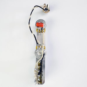 May include: A guitar wiring harness with a white and black wire, a red capacitor, a white volume knob, and a black switch.