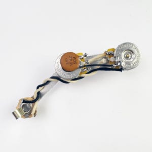 May include: A guitar wiring harness with a silver potentiometer, a brown capacitor labeled "MP 104Z 50V", and a white and black wire.