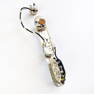 May include: A guitar wiring harness with three knobs, a switch, and wires. The harness is made of metal and has a silver finish.