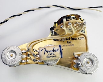 Peut inclure: Gros plan sur un faisceau de câblage de guitare couleur or avec un condensateur Fender, deux potentiomètres et un sélecteur à trois positions. Le faisceau de câblage est étiqueté "Legend-Tone.com USA STR-S-GP-BR".