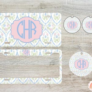 May include: A license plate, license plate frame, two car coasters, and a keychain with a floral pattern in white, blue, and pink. Each item features a pink oval with the blue initials "CHR".