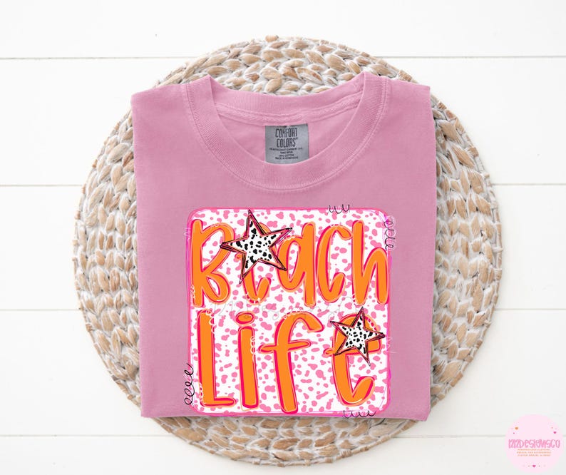 Puede incluir: Camiseta rosa con un estampado gr&aacute;fico de un dise&ntilde;o "Beach Life" rosa y naranja con estrellas blancas y negras.