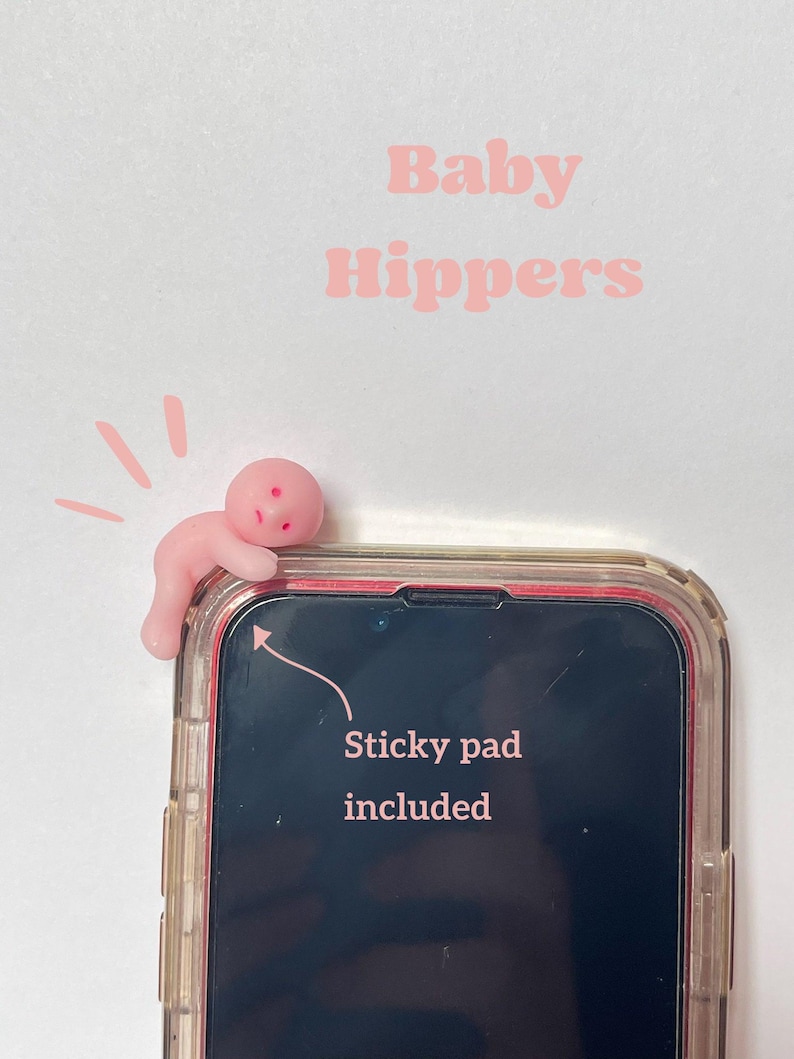 May include: A pink phone accessory shaped like a baby, attached to a phone case. The text "Baby Hippers" is above the phone. The phone screen has the text "Sticky pad included".