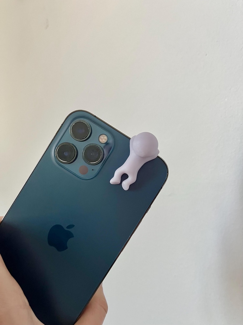 Puede incluir: Un tel&eacute;fono inteligente de color verde azulado con una peque&ntilde;a figura de color p&uacute;rpura claro adjunta. El tel&eacute;fono tiene tres lentes de c&aacute;mara y el logotipo de Apple. La figura tiene la forma de una persona.