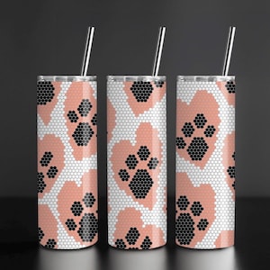 May include: Three stainless steel tumblers with a paw print design. The tumblers feature a pattern of pink hearts with black paw prints, set against a white honeycomb background. Each tumbler has a silver straw.