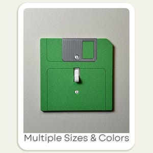 May include: A green light switch shaped like a vintage floppy disk with a white toggle switch. The switch has a gray plastic label with a blank white rectangle. The text "Multiple Sizes & Colors" is printed below the switch.