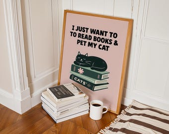 May include: A framed poster with the text "I JUST WANT TO READ BOOKS & PET MY CAT" features a black cat resting on a stack of books. A stack of books and a white mug with coffee are in front of the poster. The poster is leaning against a wall.
