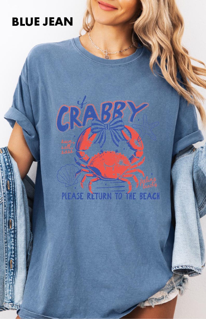 A woman wearing a blue t-shirt with a graphic design of a crab and the text "Please return to the beach" printed on it.