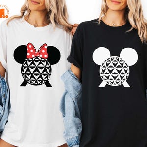 May include: Two t-shirts, one white and one black, each featuring a graphic design. The design includes a black Mickey Mouse head with white ears and a geometric sphere. The white shirt has a red bow with white polka dots.