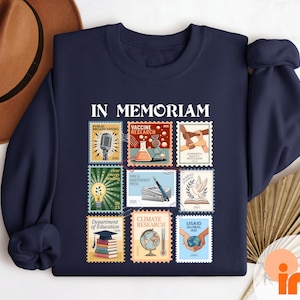 A navy blue sweatshirt with a collage of colorful postage stamps on it, along with a brown hat and a fan, all laid out on a white surface.