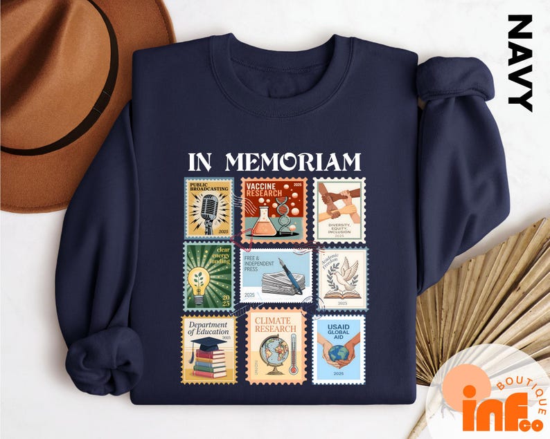 A navy blue sweatshirt with a collage of colorful postage stamps on it, along with a brown hat and a fan, all laid out on a white surface.