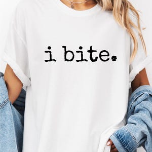 May include: White t-shirt with the phrase "i bite." printed in black. The shirt is a casual, short-sleeved style. The word "WHITE" is printed in bold, black letters at the top of the image.