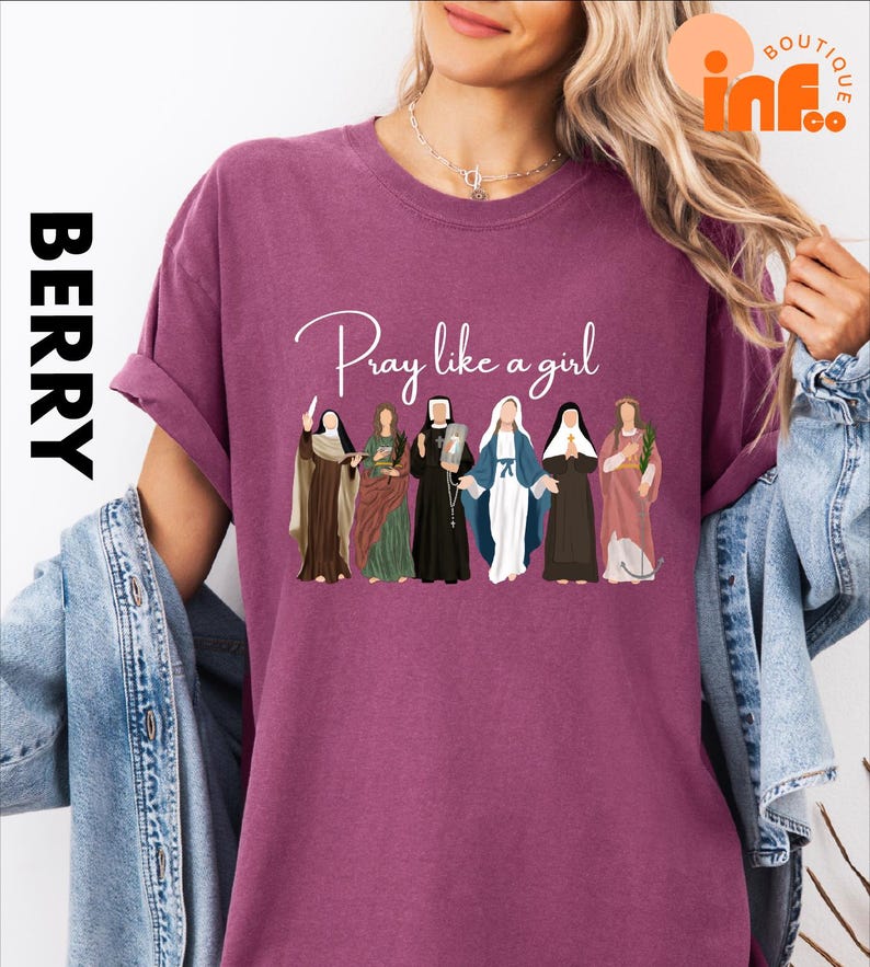 A woman wearing a purple t-shirt with a graphic design of various religious figures, including saints and religious icons, along with the text "Pray like a girl".