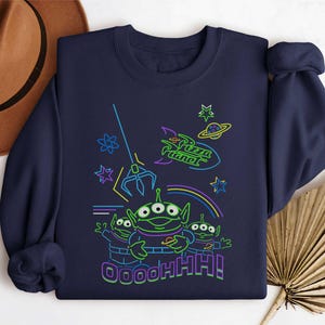 May include: Navy blue sweatshirt with a neon graphic of the Pizza Planet aliens from Toy Story. The design includes the Pizza Planet logo, a claw, stars, and the text "OOOOHHH!".