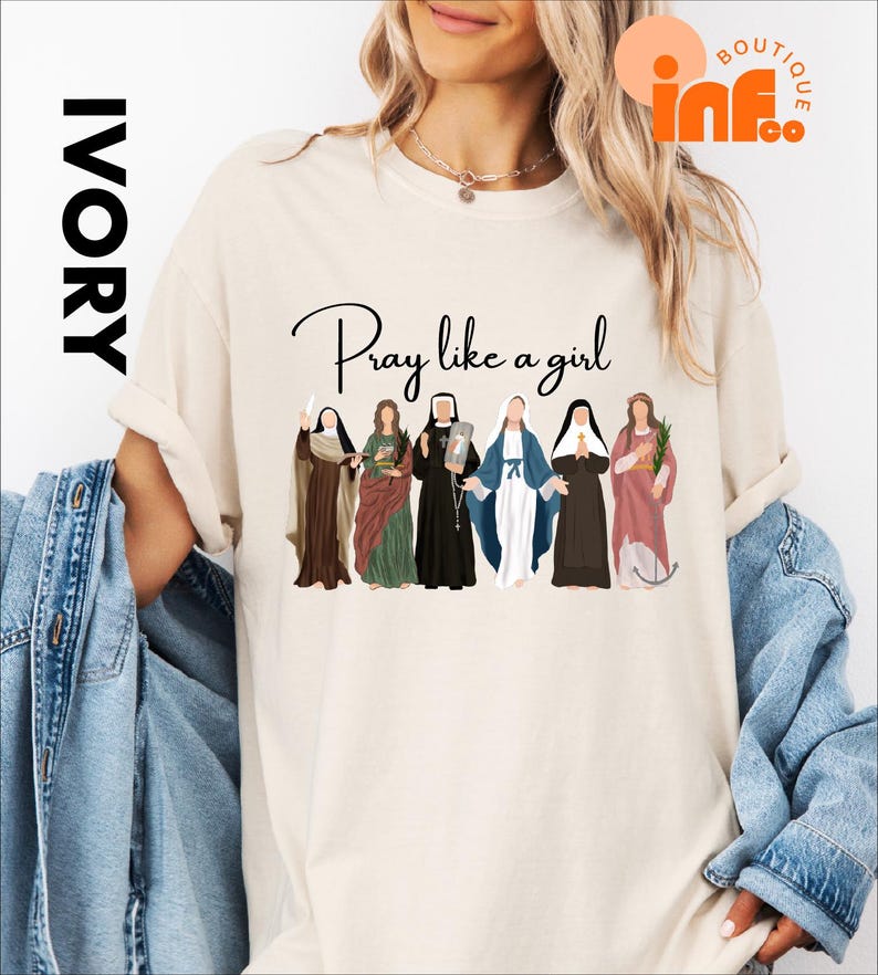 A woman wearing a white t-shirt with a graphic design of six different women in various religious attire, along with the text "Pray like a girl".