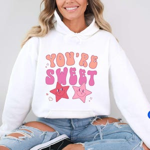 May include: White hoodie with a pink and orange graphic that says "You're Sweet" with two pink and orange stars with smiley faces.