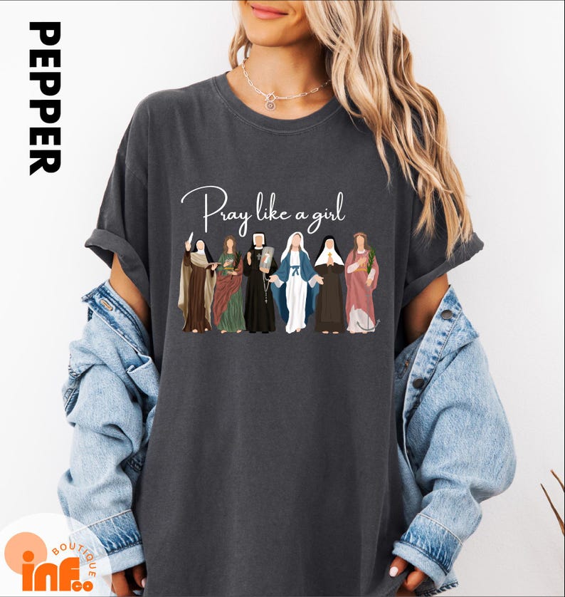 A woman wearing a gray t-shirt with a graphic design of seven different people, along with the text "Pray like a girl".