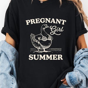 A woman wearing a black t-shirt with a graphic design of a duck and the text "Pregnant Girl Summer" printed on it.