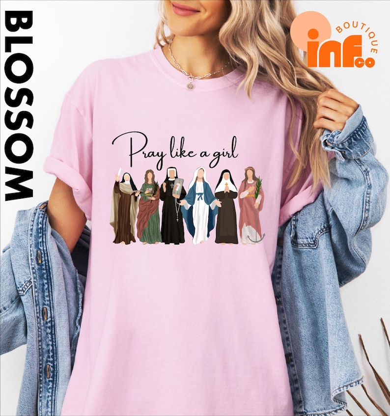 A woman wearing a pink t-shirt with a graphic design of six women in religious attire, along with the text "Pray like a girl".