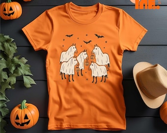 May include: An orange short-sleeve t-shirt featuring a black graphic print of four horses wearing white ghost costumes and carrying small jack-o'-lantern buckets, surrounded by black stars and bats, with a crew neckline and a standard fit.