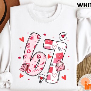 May include: White sweatshirt with a large '67' graphic in pink, decorated with hearts, envelopes, and stars. The number design includes the text '14 Feb' on a calendar. The word 'WHITE' is printed at the top.