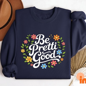 May include: Navy blue sweatshirt with the phrase "Be Pretti Good" in white script, surrounded by a floral wreath of pink, yellow, and blue flowers. The word "NAVY" is printed vertically on the right side.