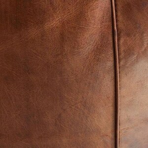 May include: Close-up of brown leather with visible grain and texture. A vertical seam runs down the center, dividing the image into two sections. The leather has a distressed appearance.